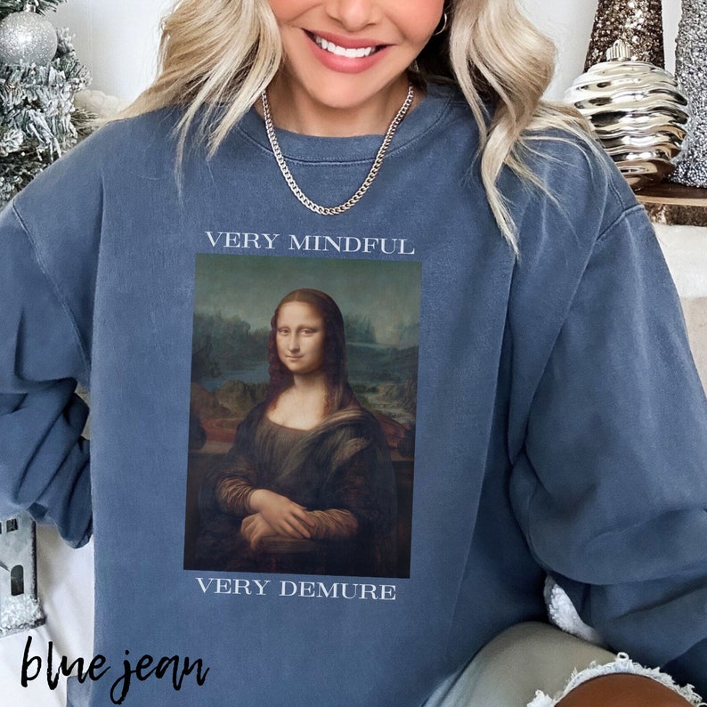 May include: A blue sweatshirt with a painting of the Mona Lisa on the front. The text "VERY MINDFUL" is above the painting and "VERY DEMURE" is below the painting.
