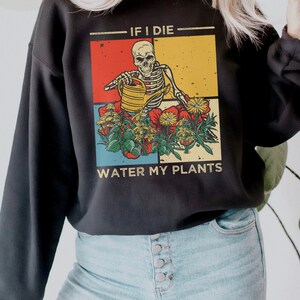 Może przedstawiać: Czarna bluza z grafiką w stylu retro przedstawiającą szkielet podlewaący rośliny. Tekst brzmi "Jeśli umrę, podlej moje rośliny."