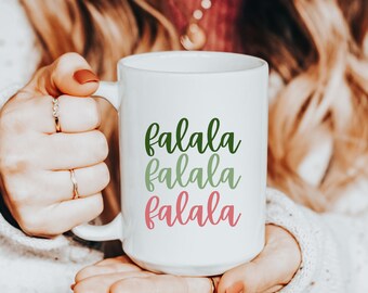 May include: White ceramic mug with the text "falala falala falala" in green and pink lettering.
