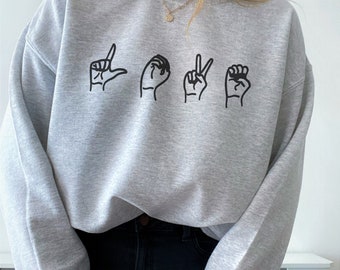May include: A gray sweatshirt with the word "LOVE" spelled out in American Sign Language.