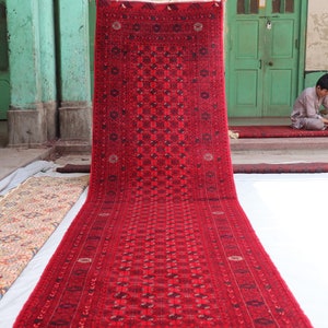 May include: A long, red rug with an intricate geometric pattern. The rug is folded in half and hanging from a wall.