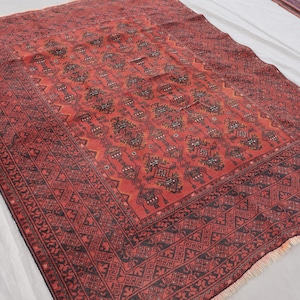 Pode incluir: Um tapete oriental retangular vermelho com um padr&atilde;o geom&eacute;trico detalhado em preto e vermelho escuro. O tapete tem um design de medalh&atilde;o central e uma borda estampada. O tapete &eacute; exibido em uma superf&iacute;cie branca.