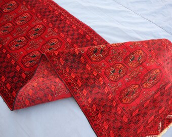 Puede incluir: Una vibrante alfombra roja con intrincados patrones geométricos y un borde detallado. La alfombra está doblada, mostrando el diseño y la textura. El diseño de la alfombra presenta formas octogonales repetidas y probablemente está hecha de lana.