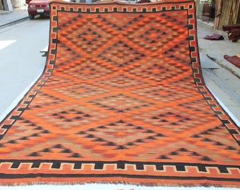May include: A large rectangular area rug featuring a vibrant orange background with a repeating pattern of black and tan diamonds. The rug is bordered by a thick black geometric frame and finished with a short fringe along the bottom edge.