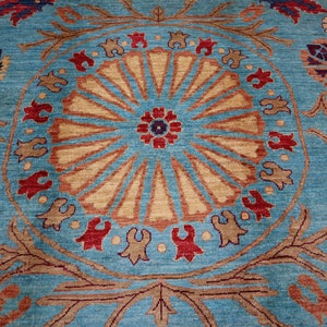 May include: A blue rug with a large, intricate, circular pattern in shades of brown, red, and beige. The pattern features a central flower motif surrounded by radiating lines and smaller floral designs.