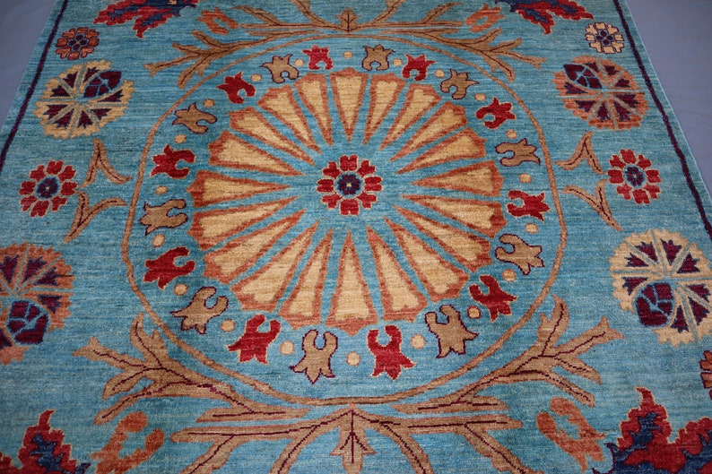 May include: A blue rug with a large, intricate, circular pattern in shades of brown, red, and beige. The pattern features a central flower motif surrounded by radiating lines and smaller floral designs.