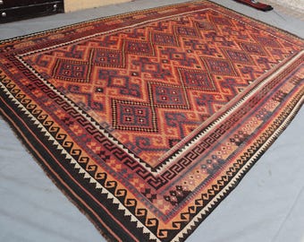 May include: A rectangular rug with a geometric pattern in shades of red, orange, and blue. The rug has a black border with white and orange triangular accents. The central design features repeating diamond shapes.