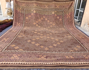 May include: A large rectangular area rug featuring a deep brown base color with intricate geometric patterns in lighter tan and muted purple tones. The design includes a central diamond grid, repeating floral motifs, and a wide decorative border.