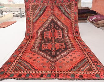 May include: A vintage Turkish rug with a red, orange, and black geometric pattern. The rug has a fringed edge and is made of wool.