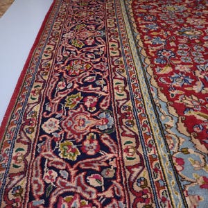 May include: A rectangular area rug featuring a deep red field with intricate floral and vine patterns in shades of blue, cream, and pink. The wide border displays a dark navy background with elaborate scrolling motifs in red and light blue.