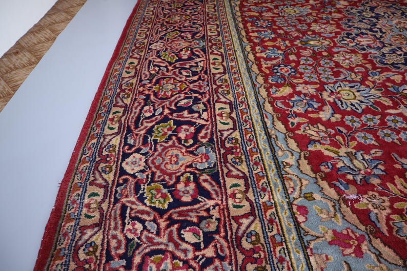 May include: A rectangular area rug featuring a deep red field with intricate floral and vine patterns in shades of blue, cream, and pink. The wide border displays a dark navy background with elaborate scrolling motifs in red and light blue.