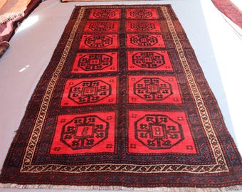 Puede incluir: Una alfombra rectangular con un fondo rojo vibrante y un patrón repetitivo de medallones octogonales negros. La alfombra está enmarcada por un borde oscuro con motivos geométricos complejos y terminada con flecos blancos cortos en ambos extremos.