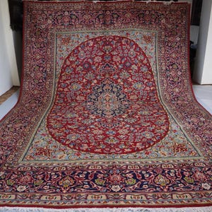 May include: A large rectangular area rug featuring a central dark blue medallion set against a vibrant red field filled with intricate floral and vine patterns. The rug is framed by a wide, ornate border in deep blue, red, and cream tones.