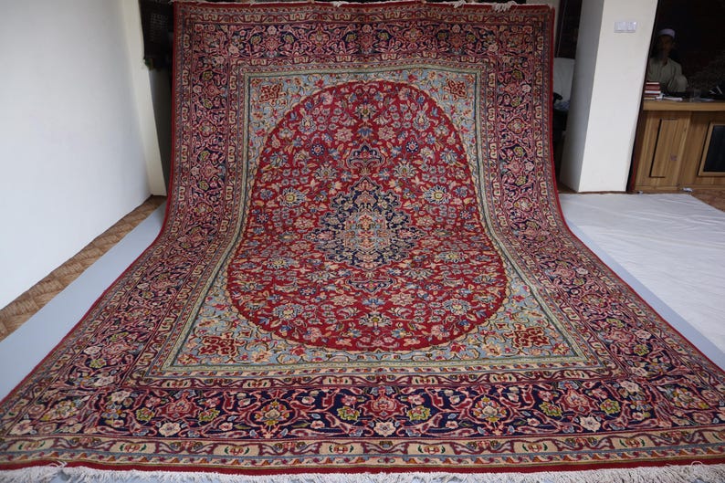 May include: A large rectangular area rug featuring a central dark blue medallion set against a vibrant red field filled with intricate floral and vine patterns. The rug is framed by a wide, ornate border in deep blue, red, and cream tones.