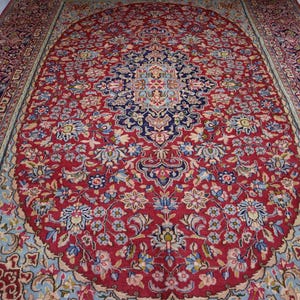 May include: A rectangular area rug featuring a deep red central field with an intricate navy blue and light blue floral medallion. The border displays a complex pattern of repeating floral motifs in shades of red, navy, and light blue.