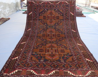 Puede incluir: Una alfombra persa tradicional con fondo azul oscuro y intrincados patrones geométricos en tonos rojos, naranjas y marrones. La alfombra está doblada por la mitad y colocada sobre una superficie blanca.