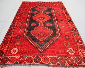 Puede incluir: Una alfombra roja con un patrón geométrico negro y rojo. La alfombra tiene un borde de flecos.