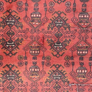 Pode incluir: Close-up de um tapete vermelho com um padr&atilde;o geom&eacute;trico repetitivo em preto, branco e dourado. O design apresenta formas estilizadas e motivos florais. O tapete tem uma apar&ecirc;ncia desgastada.
