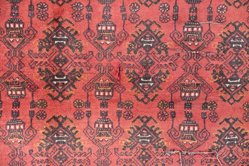 Pode incluir: Close-up de um tapete vermelho com um padr&atilde;o geom&eacute;trico repetitivo em preto, branco e dourado. O design apresenta formas estilizadas e motivos florais. O tapete tem uma apar&ecirc;ncia desgastada.