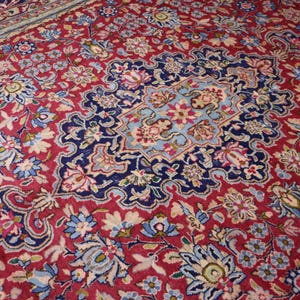 May include: A rectangular area rug featuring a deep red background with an intricate floral pattern in shades of navy blue, light blue, white, and pink. The design includes a central medallion surrounded by dense botanical motifs and vines.