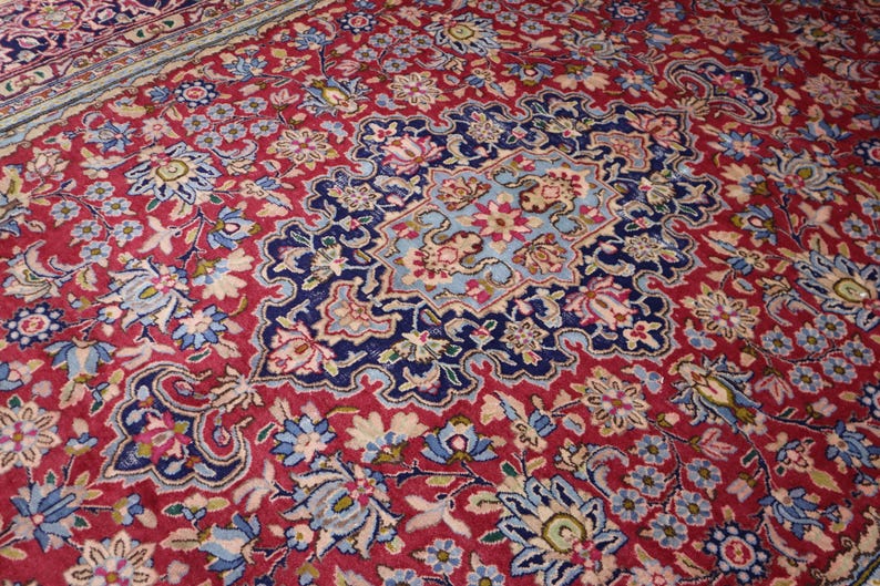 May include: A rectangular area rug featuring a deep red background with an intricate floral pattern in shades of navy blue, light blue, white, and pink. The design includes a central medallion surrounded by dense botanical motifs and vines.