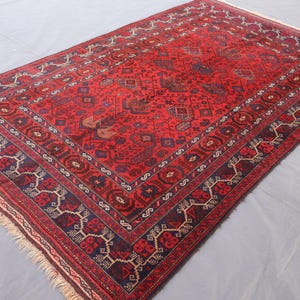 May include: A rectangular, red oriental rug with a detailed geometric pattern. The rug features a central field of red with intricate designs in navy blue, brown, and cream. A navy blue border frames the rug, adding contrast.