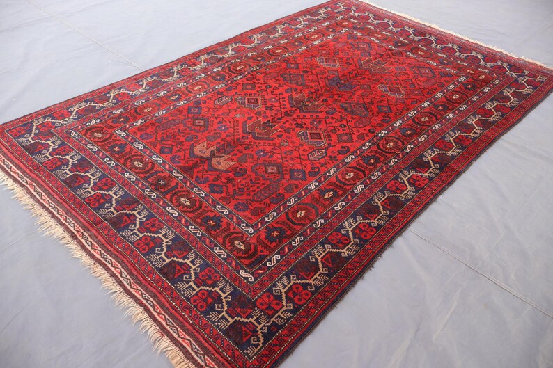 May include: A rectangular, red oriental rug with a detailed geometric pattern. The rug features a central field of red with intricate designs in navy blue, brown, and cream. A navy blue border frames the rug, adding contrast.