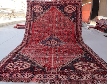 Puede incluir: Una alfombra vintage roja y azul con un patrón geométrico. La alfombra tiene un borde de flecos y está hecha de lana.