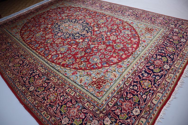 May include: A rectangular area rug featuring a central dark blue medallion surrounded by a red field filled with intricate floral and vine patterns. The border displays a complex design of flowers and leaves in shades of red, blue, and cream.