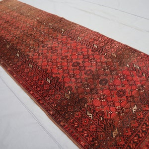 Peut inclure: Un tapis de couloir rouge et noir avec un motif persan traditionnel. Le tapis a des franges aux deux extrémités.