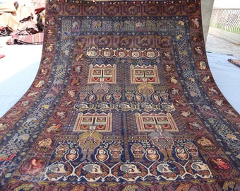 May include: A vintage Persian rug with a dark blue background and intricate patterns. The rug features a central design of four windows with figures inside, surrounded by a border of stylised animals and plants.