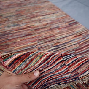 May include: A colorful handwoven rug with a striped pattern in shades of red, blue, green, and beige. The rug has a fringe border and is folded in half.
