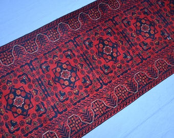 Op de afbeelding: Een rood, zwart en wit gestreept tapijt met een geometrisch ontwerp. Het tapijt heeft een traditionele Perzische stijl.