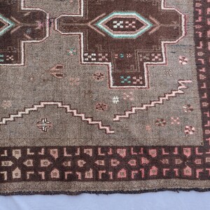 K&ouml;nnte beinhalten: Nahaufnahme eines Teils eines Vintage-Teppichs mit geometrischem Muster. Der Teppich hat eine braune und graue Farbpalette mit Akzenten in T&uuml;rkis und Rosa. Das Design umfasst sich wiederholende Formen und einen Fransenrand.