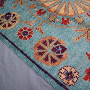 May include: A teal blue rug with a large, intricate, circular pattern in the center. The pattern is made up of beige, orange, red, and purple colors. The rug has a border of smaller floral patterns in the same colors.