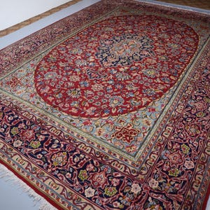 May include: A large rectangular area rug featuring a central red oval medallion filled with intricate floral patterns in blue, cream, and gold. The surrounding field is light blue, framed by a wide dark blue border with dense floral motifs.
