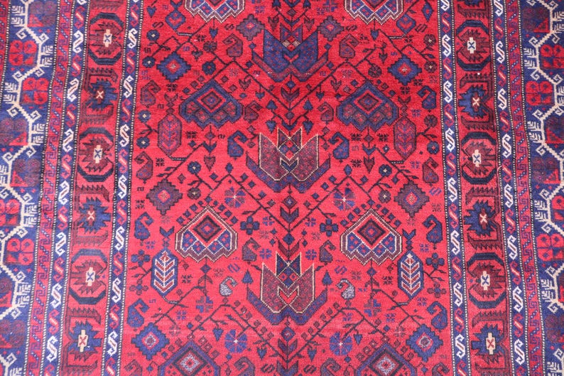 May include: A red and blue patterned rug with a central design of stylized floral and geometric shapes. The rug features a repeating pattern with a border of alternating shapes and colors. The rug is likely made of wool.