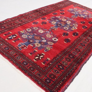 May include: A red rug with a traditional Persian design featuring intricate floral patterns and a dark blue border. The rug has a rich, vibrant color and a soft, luxurious feel.