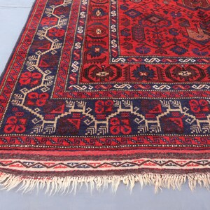 May include: A red and navy blue patterned rug with a detailed border and fringe. The rug features geometric designs in shades of red, navy blue, and beige. The rug's dimensions are not visible in the image.
