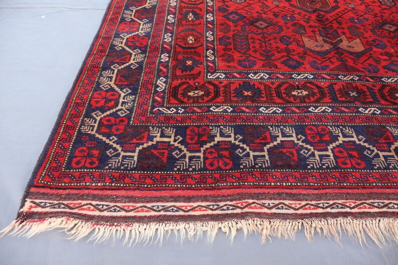May include: A red and navy blue patterned rug with a detailed border and fringe. The rug features geometric designs in shades of red, navy blue, and beige. The rug's dimensions are not visible in the image.