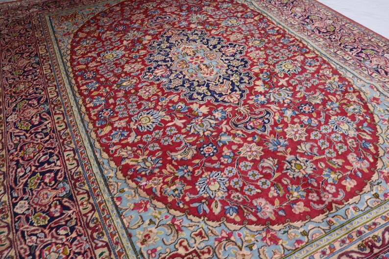 May include: A rectangular area rug featuring a deep red central field with an intricate floral pattern in shades of blue, cream, and pink. The rug has a prominent dark blue central medallion and a wide, detailed border with complex floral motifs.