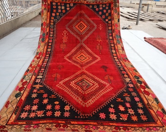May include: A red, black, and orange patterned rug with a diamond design. The rug is folded in half and laid out on a white surface.