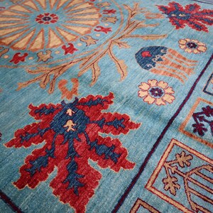 May include: A blue rug with a traditional Persian design. The rug features a central medallion with floral motifs and a border with geometric patterns. The colors are vibrant and include shades of blue, red, and gold.