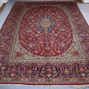 May include: A large rectangular area rug featuring a deep red central field with an intricate navy blue and cream floral medallion. The border displays complex botanical patterns in shades of red, navy, cream, and light blue with white fringe.