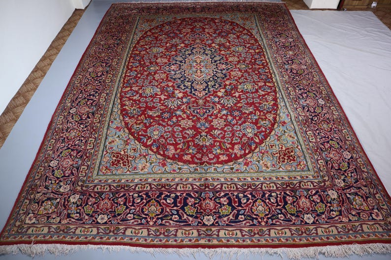 May include: A large rectangular area rug featuring a deep red central field with an intricate navy blue and cream floral medallion. The border displays complex botanical patterns in shades of red, navy, cream, and light blue with white fringe.