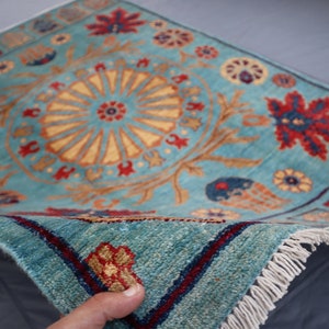 May include: A blue rug with a floral pattern and a central medallion. The rug has a fringe border and is folded in half.