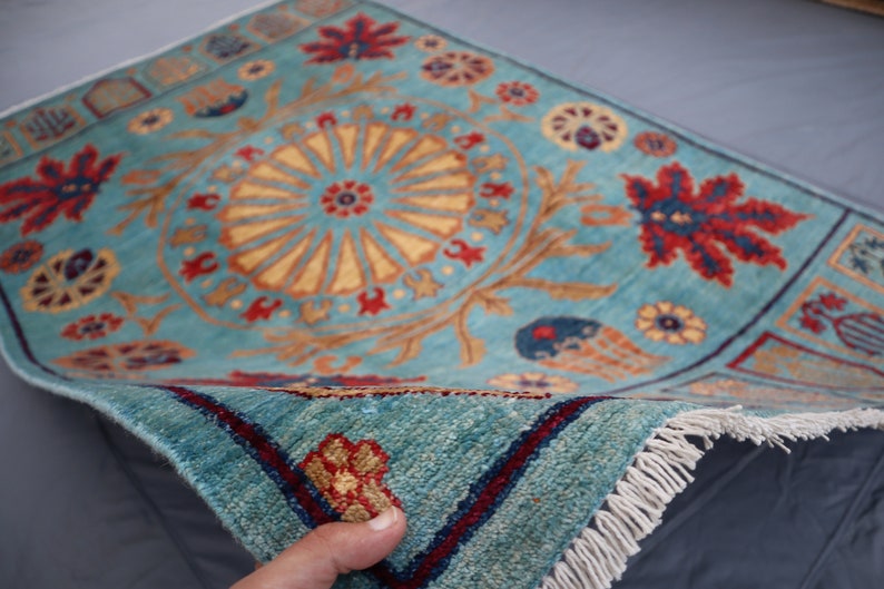 May include: A blue rug with a floral pattern and a central medallion. The rug has a fringe border and is folded in half.