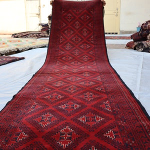 May include: A red and black patterned rug with a geometric design. The rug is being held up by a person's hands.