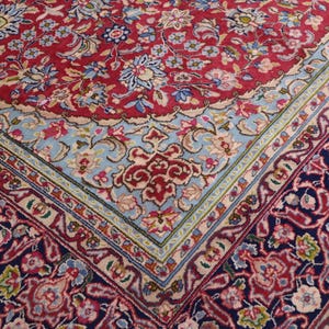 May include: A rectangular area rug featuring a dense floral pattern in shades of red, navy blue, and light blue. The design includes a central field with intricate botanical motifs, surrounded by a wide border with repeating floral elements.