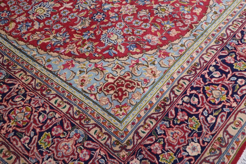 May include: A rectangular area rug featuring a dense floral pattern in shades of red, navy blue, and light blue. The design includes a central field with intricate botanical motifs, surrounded by a wide border with repeating floral elements.